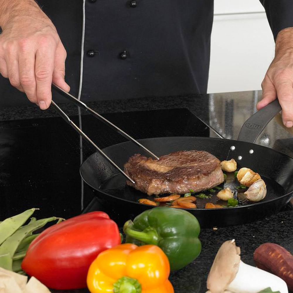 Uno chef gira una bistecca in padella con aglio e carote.