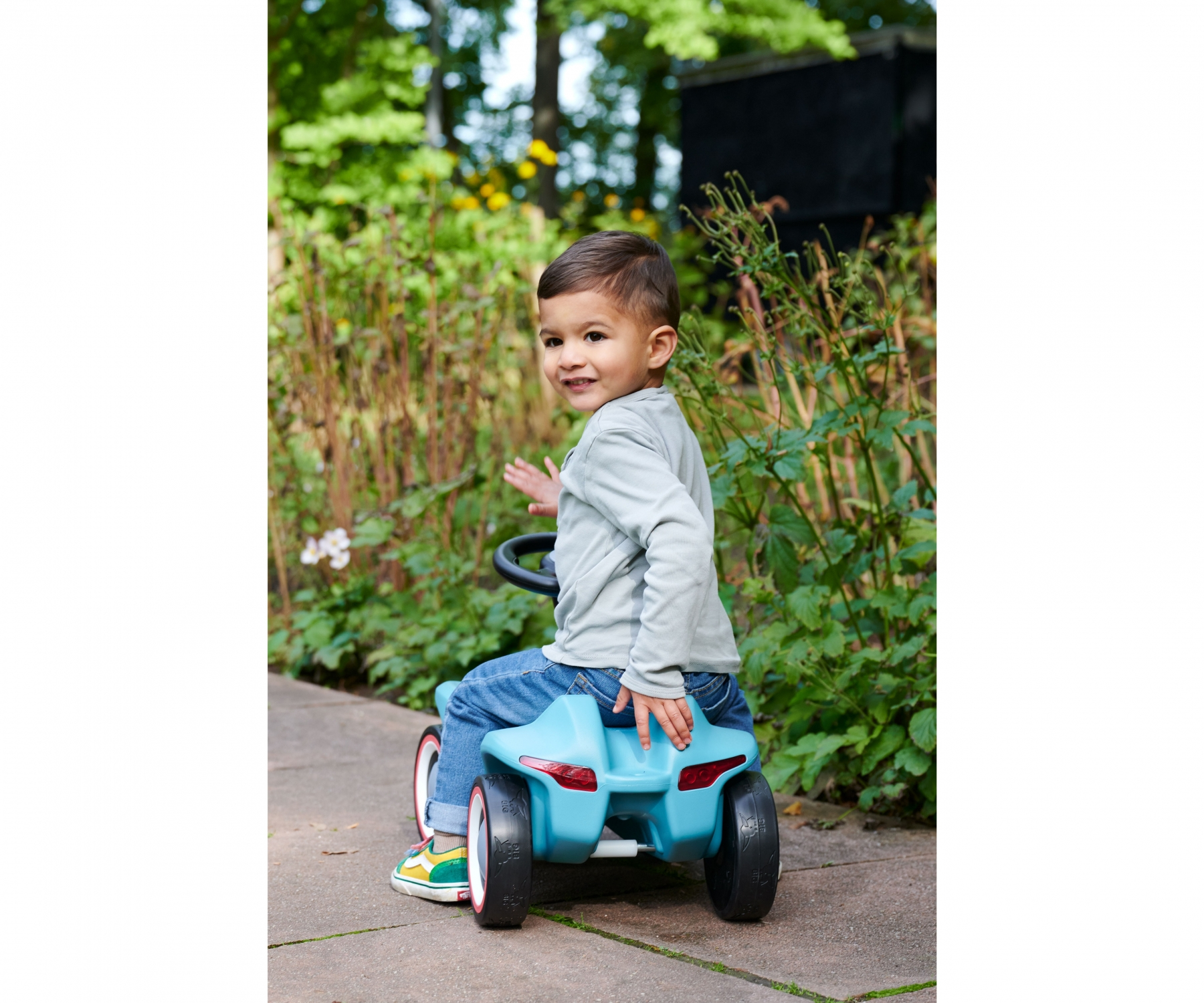 Ein kleiner Junge sitzt auf einem blauen Spielzeugauto im Freien.