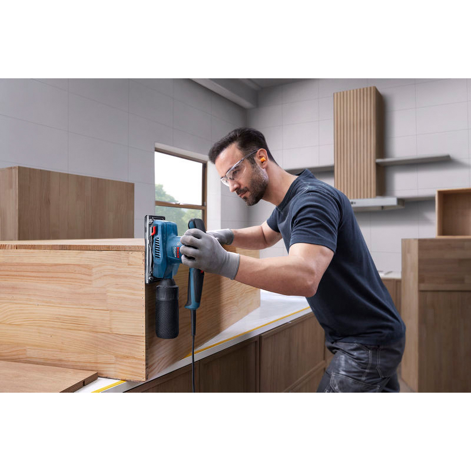 Mann schleift Holzmöbel mit blauem Exzenterschleifer, trägt Schutzbrille und Handschuhe.