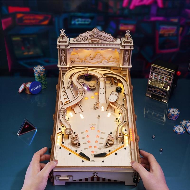 Ein hölzernes Flipper-Modell mit Lichtern, Chips und Spielautomaten im Hintergrund.