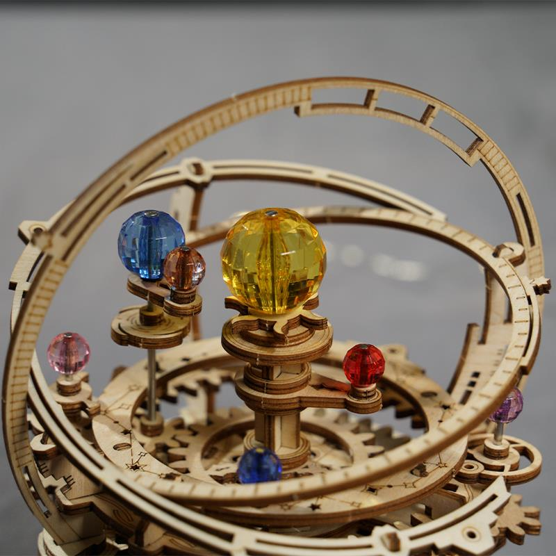 Ahşap orrery modeli, kollarda renkli cam gezegenler, gri arka plan.