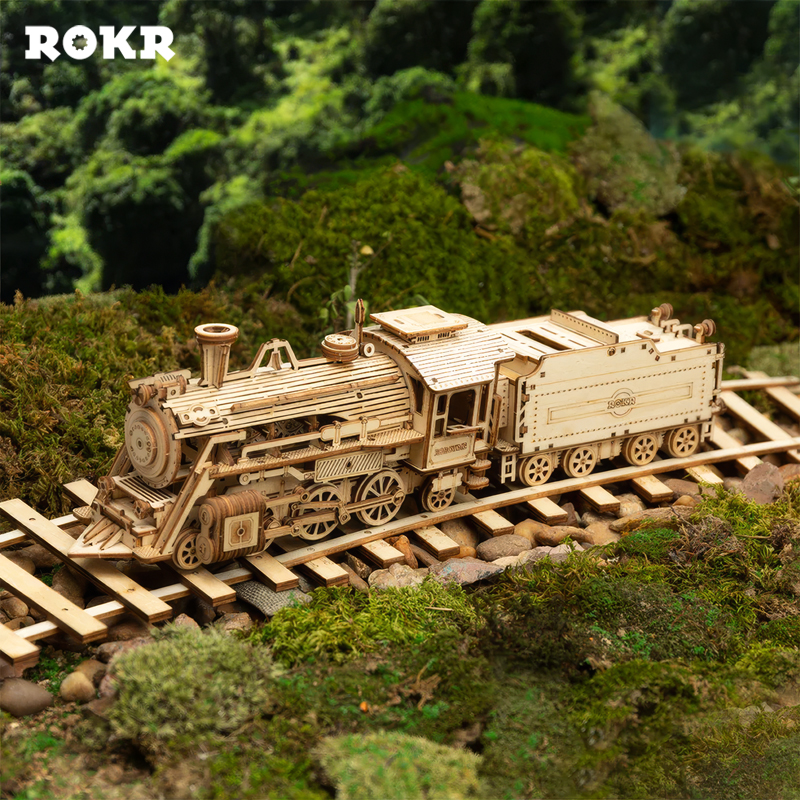 Ahşap model tren, yeşil yosunla çevrili raylarda.