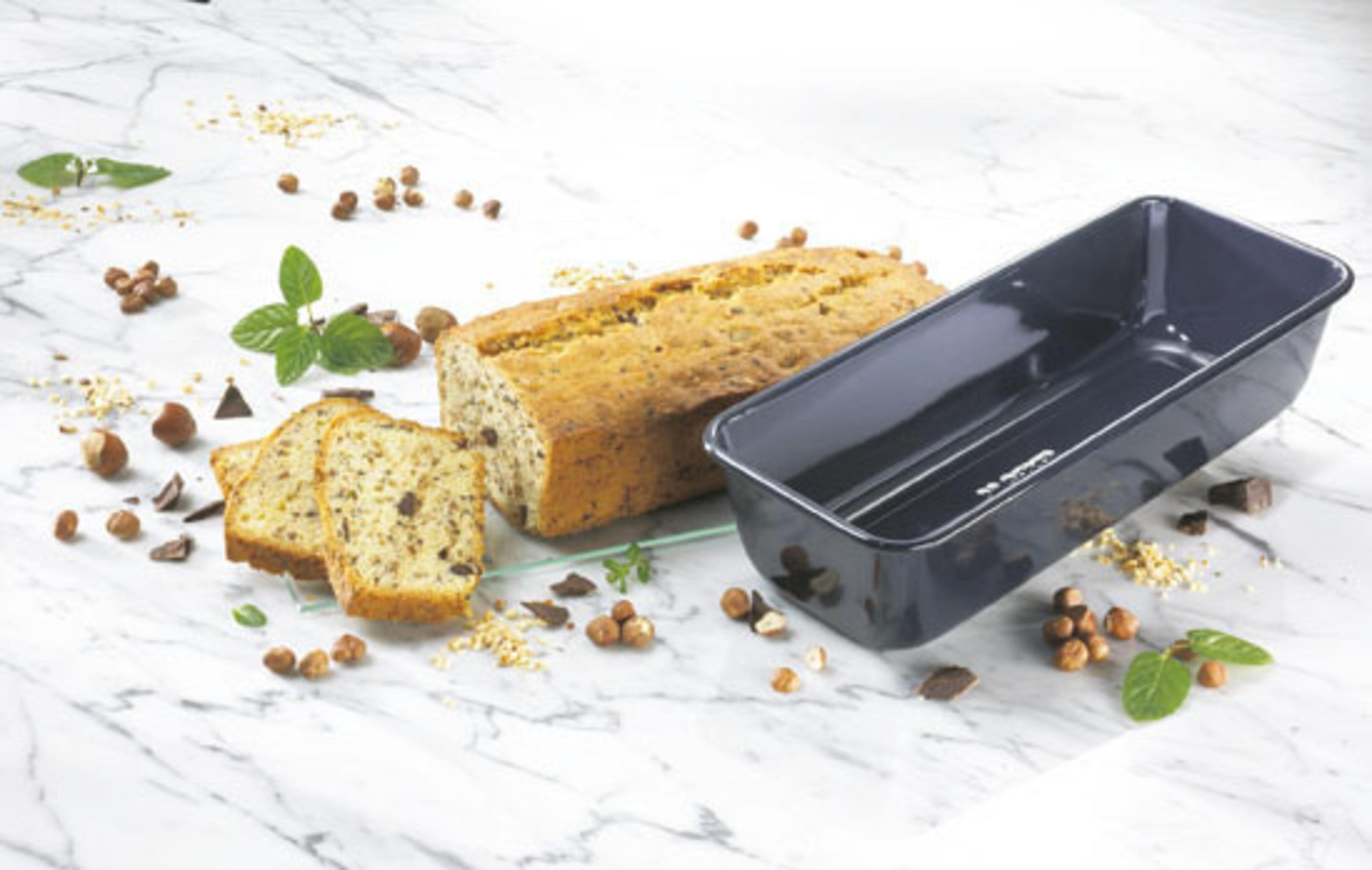 Ein Laib Brot mit drei Scheiben, neben einer dunklen Backform, Nüssen und Minze.