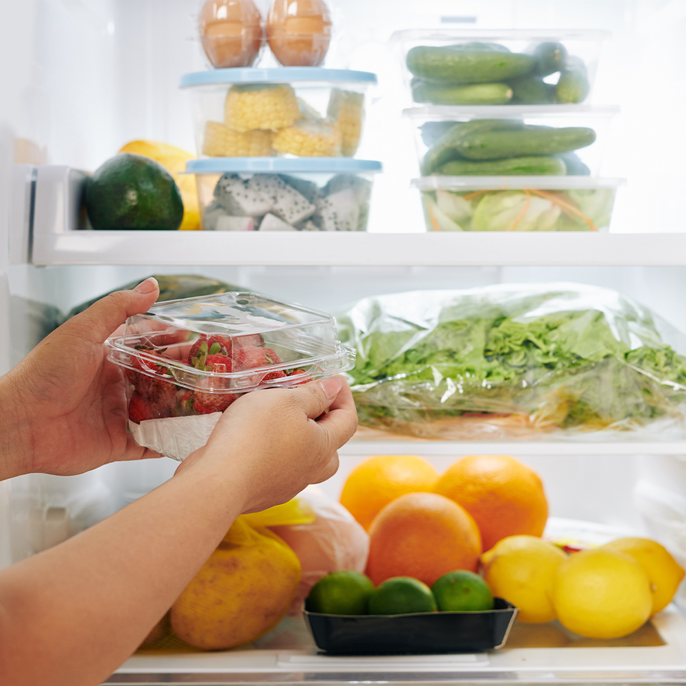 Manos sosteniendo un recipiente con fresas en un refrigerador con frutas y verduras.