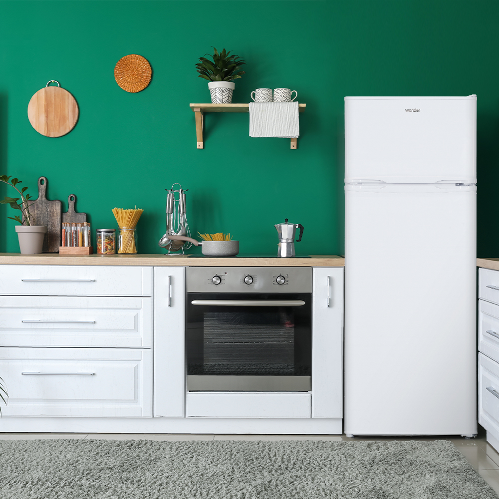 Una cocina verde con gabinetes blancos, horno, nevera, utensilios y pasta.