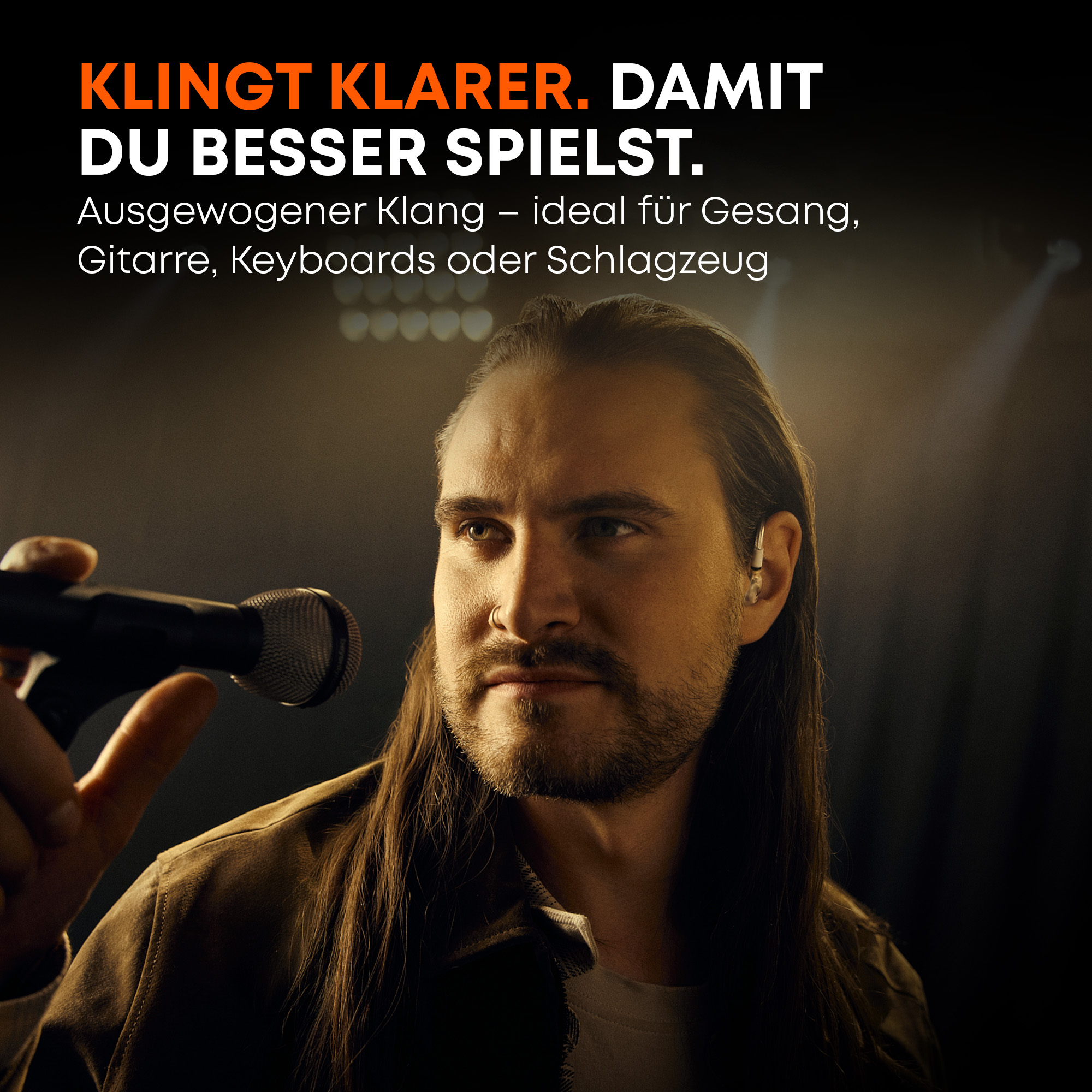 Ein Mann mit langen Haaren hält ein Mikrofon, er trägt einen In-Ear-Monitor.