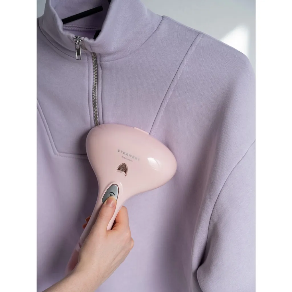Eine Hand hält einen rosa Dampfglätter, der einen lila Pullover glättet.