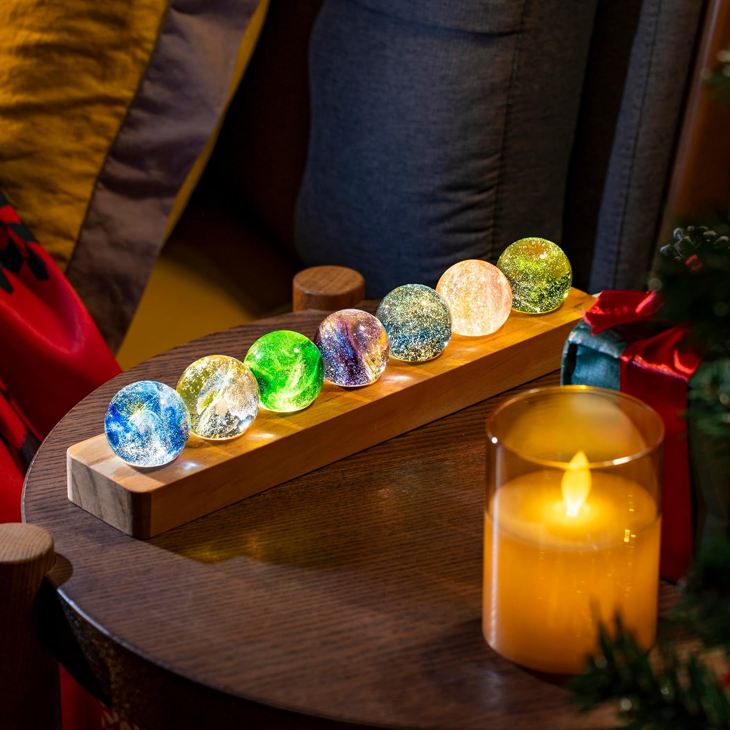 Leuchtende Kugeln mit Glitzer auf Holzständer, neben Kerze.