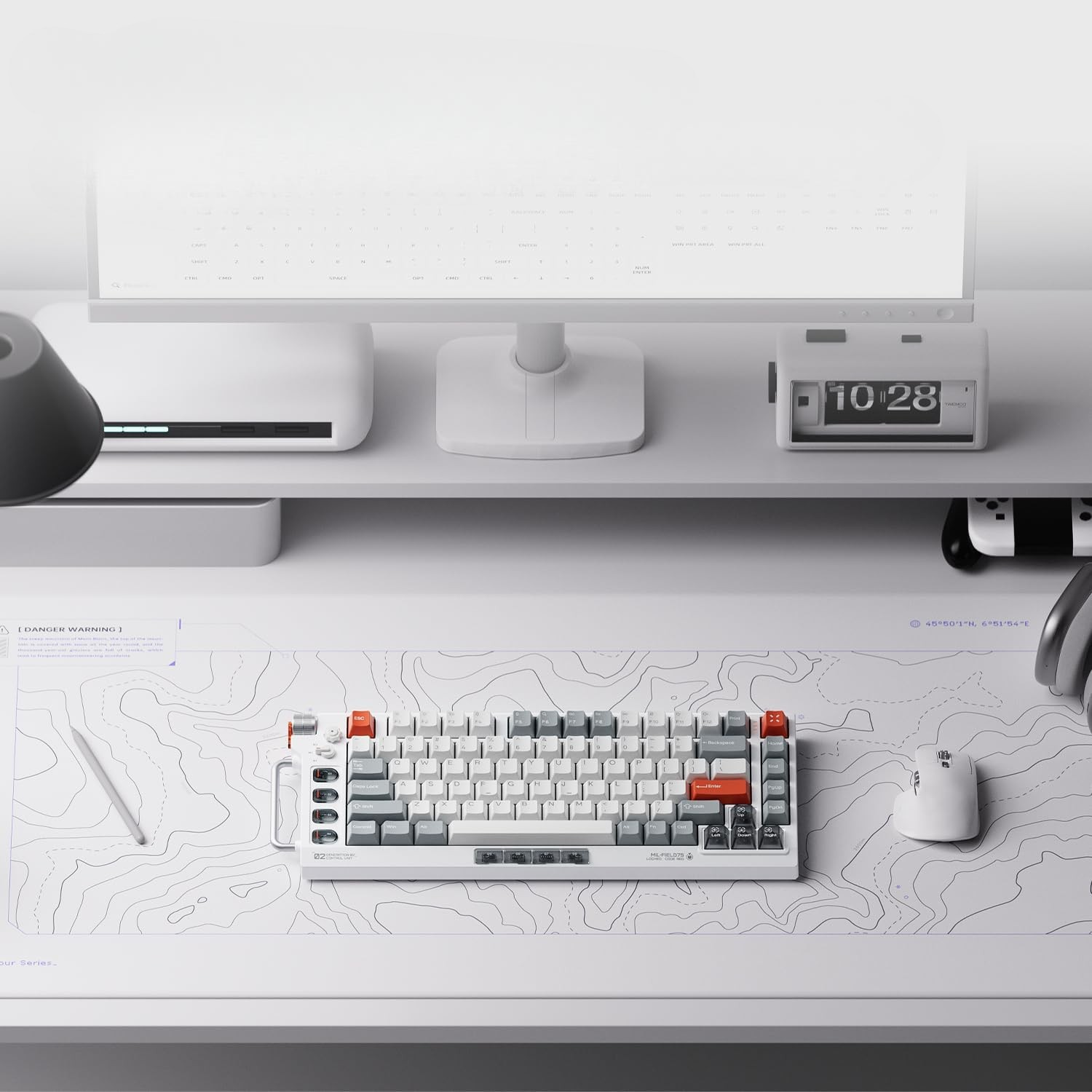 Biała klawiatura z czerwonymi akcentami na macie topograficznej. W pobliżu biała mysz i monitor.