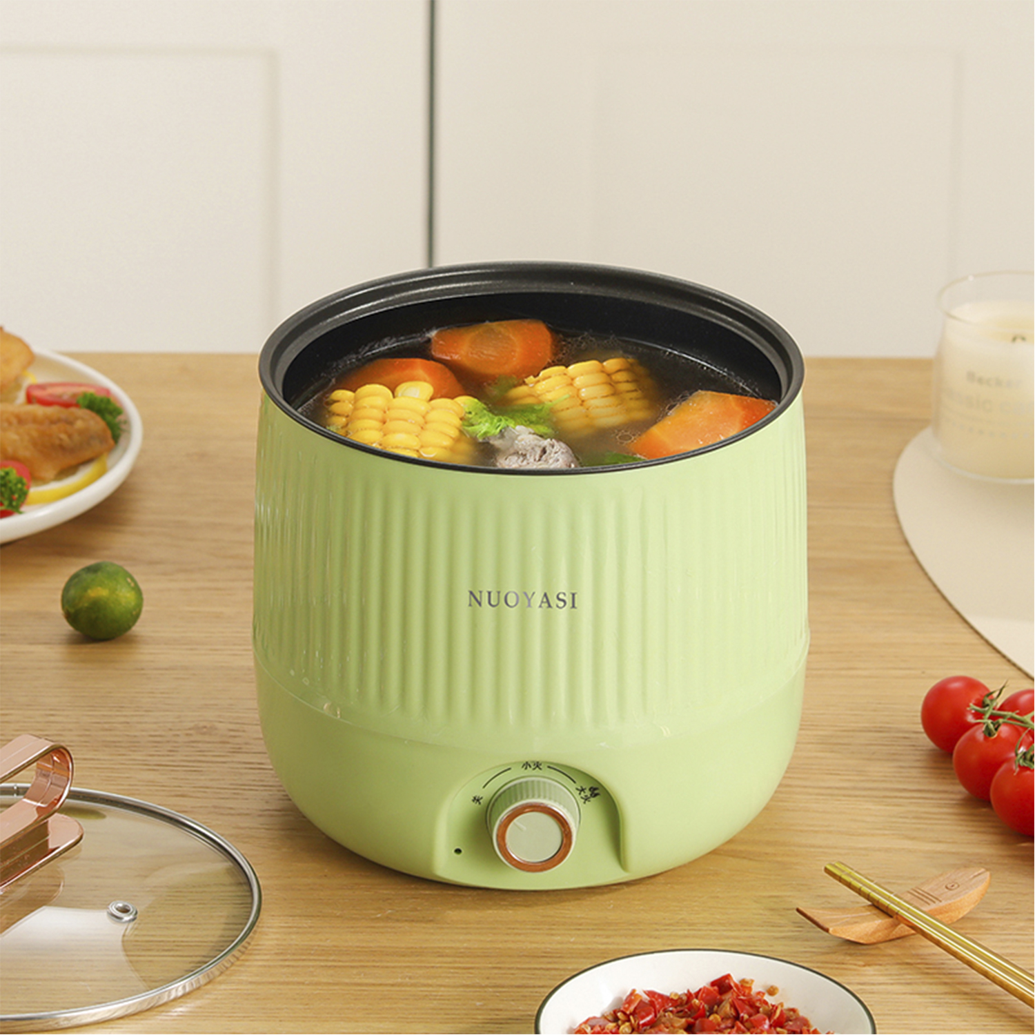 Una pentola elettrica verde con mais, carote e carne in brodo. Tavola apparecchiata con cibo.