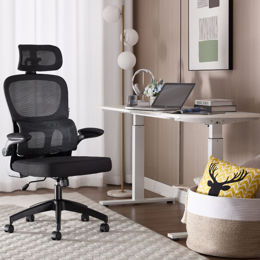 Sedia da ufficio nera in rete davanti a una scrivania regolabile in altezza con laptop e decorazioni.
