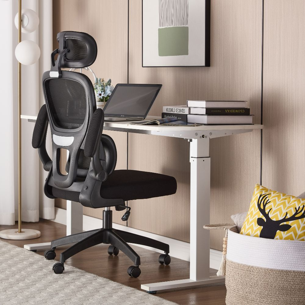 Una sedia da ufficio ergonomica nera davanti a una scrivania bianca regolabile in altezza.