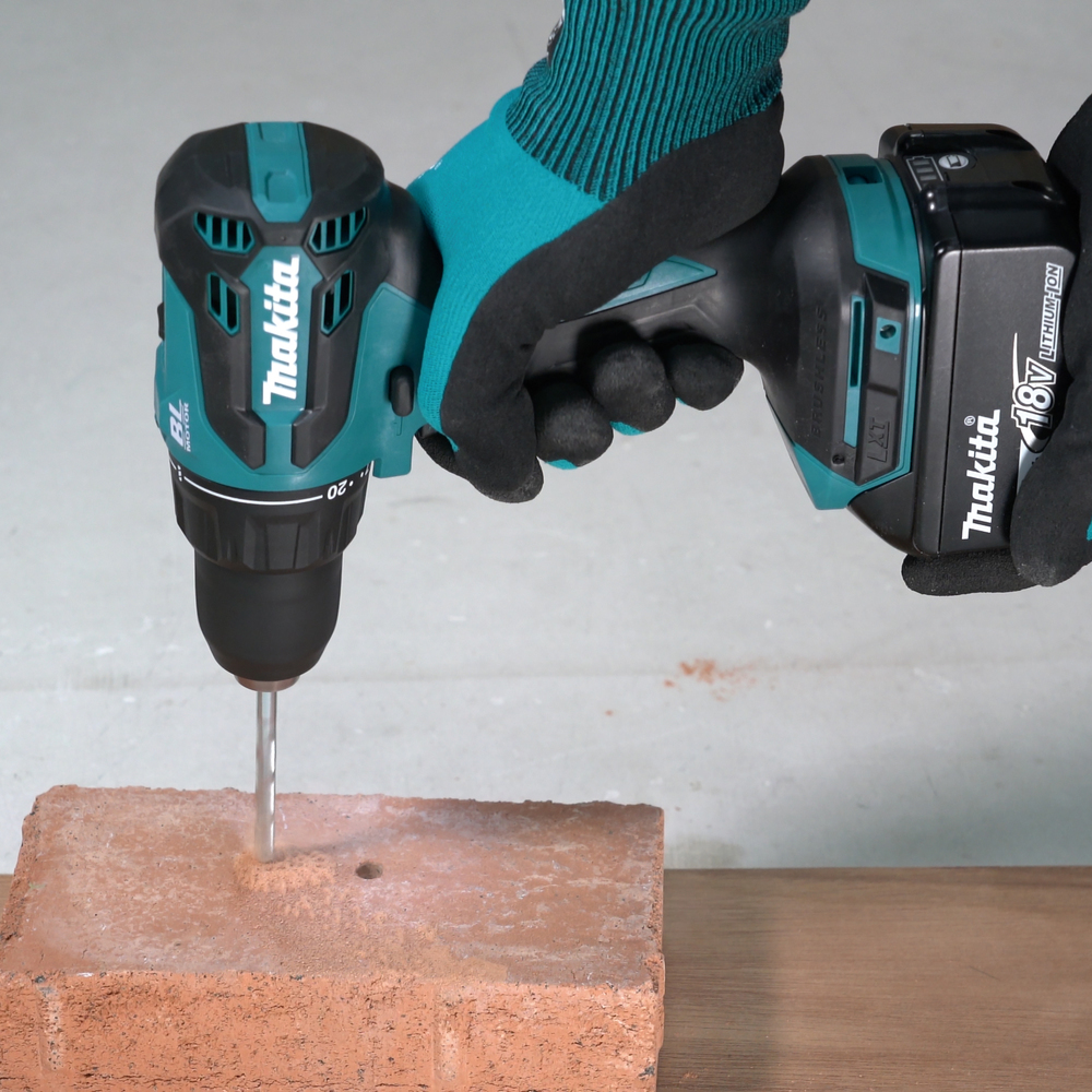 Person mit Handschuhen bohrt mit Makita Akku-Bohrer in roten Ziegel.