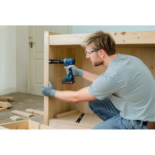 Ein Mann mit Schutzbrille und Handschuhen montiert mit einem Akku-Bohrer Holzmöbel.