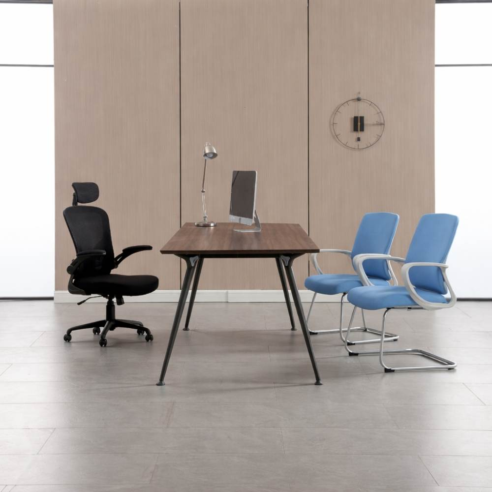 Una sedia da ufficio nera e due sedie blu sono a un tavolo di legno con computer e lampada.