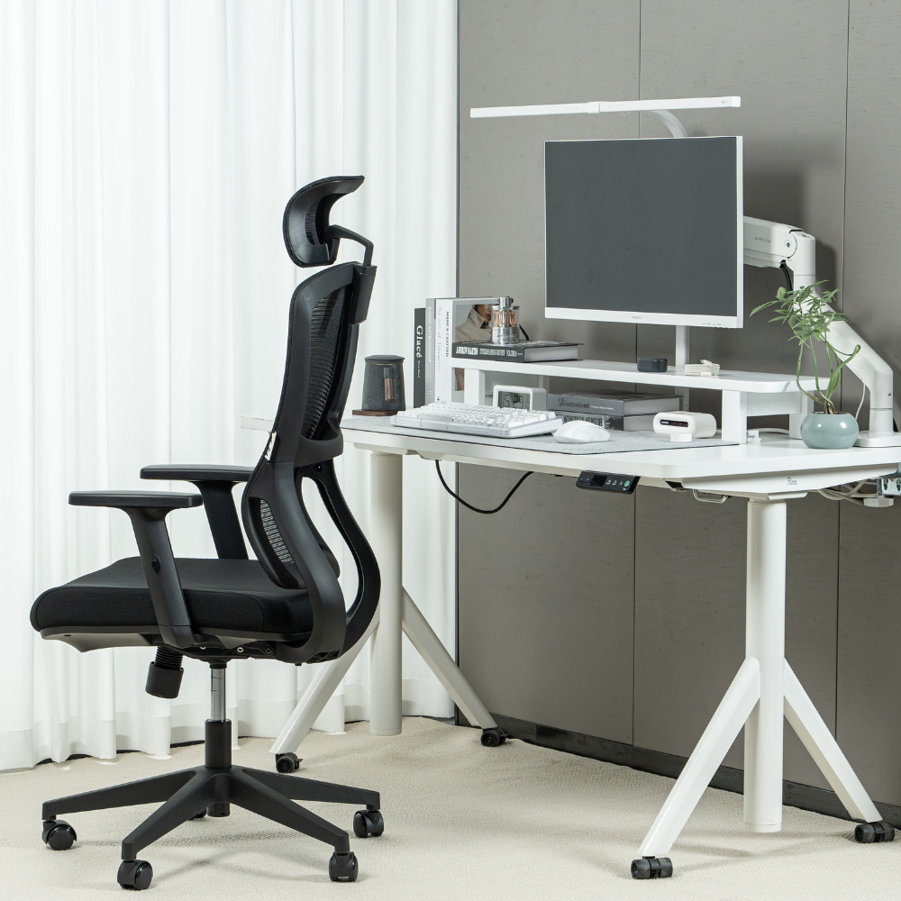 Sedia da ufficio ergonomica in rete nera accanto a una scrivania bianca regolabile con computer.
