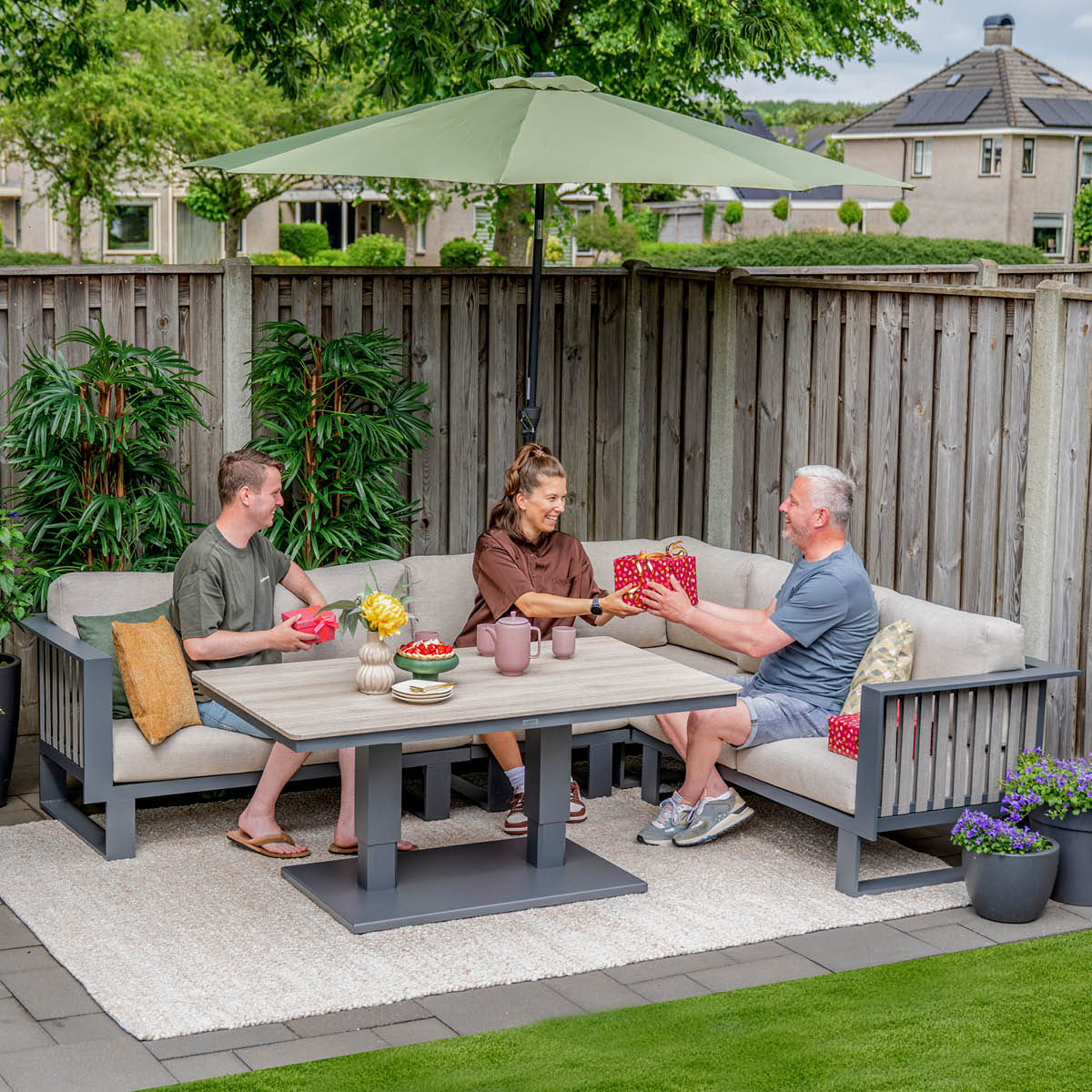 Drie mensen zitten op een loungeset in de tuin en wisselen cadeaus uit.