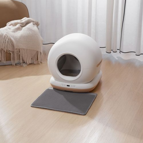 Eine weiße, kugelförmige automatische Katzentoilette steht auf einer grauen Matte auf Holzboden.