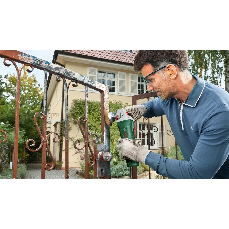 Hombre usando amoladora para limpiar puerta oxidada frente a casa.