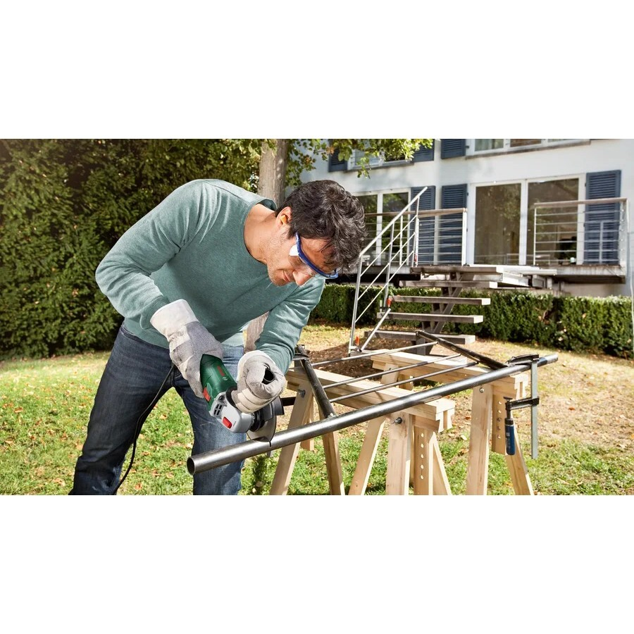 Hombre con gafas y guantes corta tubo metalico con amoladora en jardin.