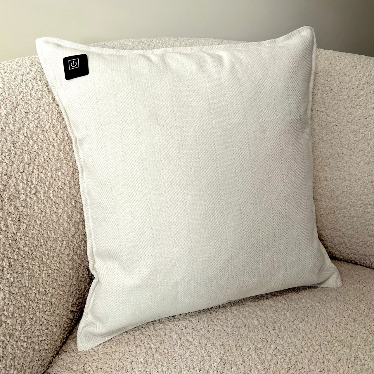 Ein weißes Kissen mit Fischgrätmuster auf einem strukturierten Sofa. Links ist ein schwarzes Quadrat mit einem Power-Symbol.