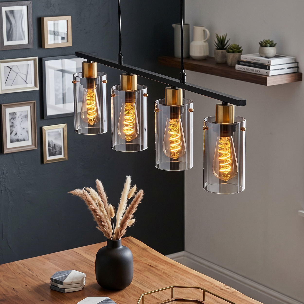 Ein moderner Kronleuchter mit vier Glasschirmen hängt über einem Holztisch mit einer Vase mit Trockenblumen.