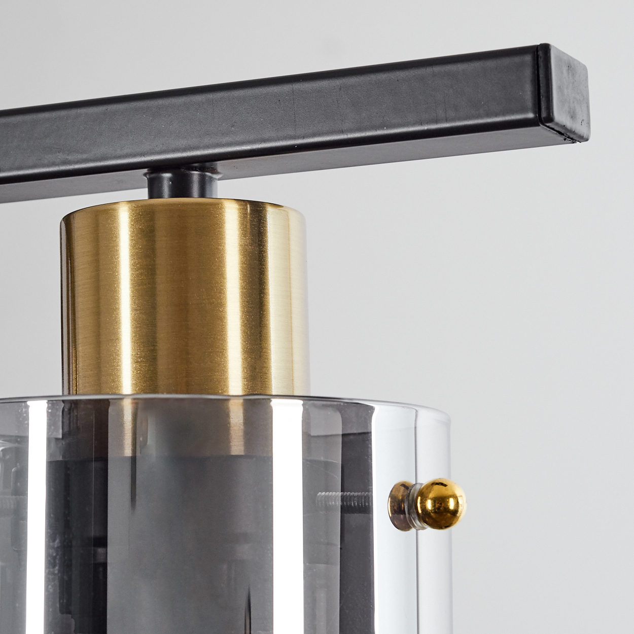 Ein schwarzer Balken über einem goldenen Zylinder und einem grauen Glaszylinder.
