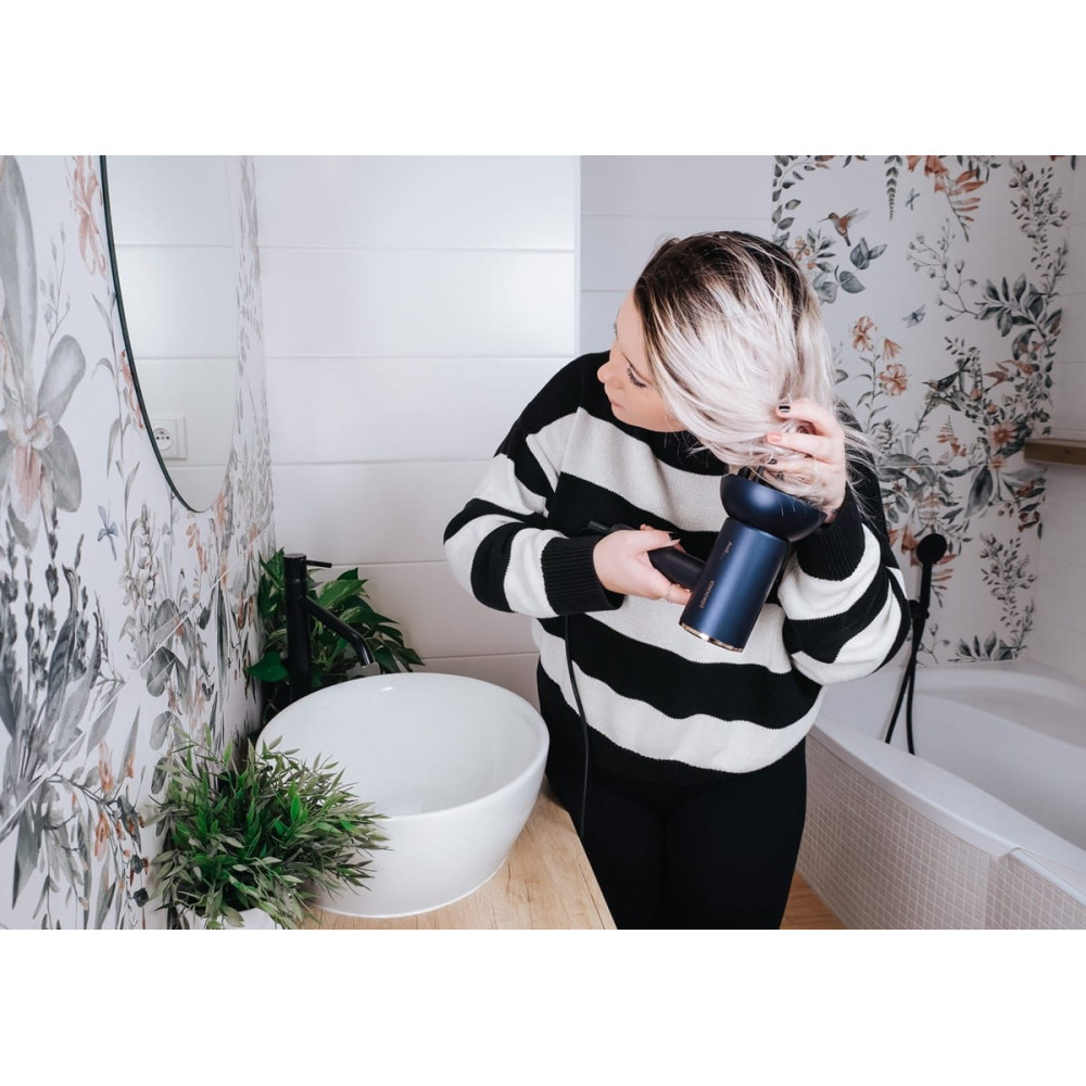 Kobieta suszy blond włosy w łazience niebieską suszarką.