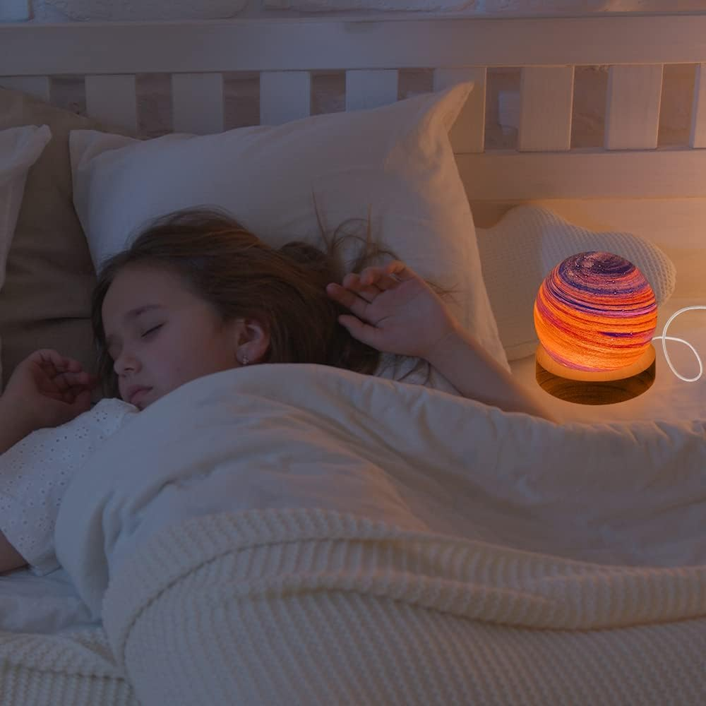 Ein Mädchen schläft im Bett neben einer bunten Lampe.