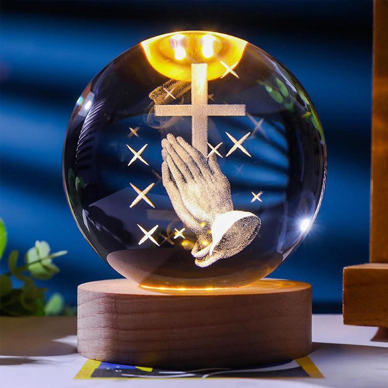 Kristallkugel mit betenden Händen und Kreuz, von unten beleuchtet.