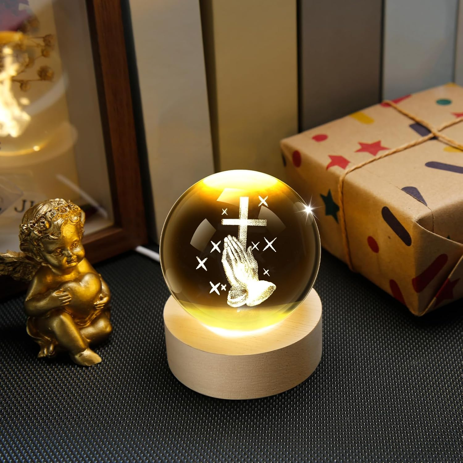 Goldene Engelsfigur hält Herz, leuchtende Kristallkugel mit betenden Händen und Kreuz.