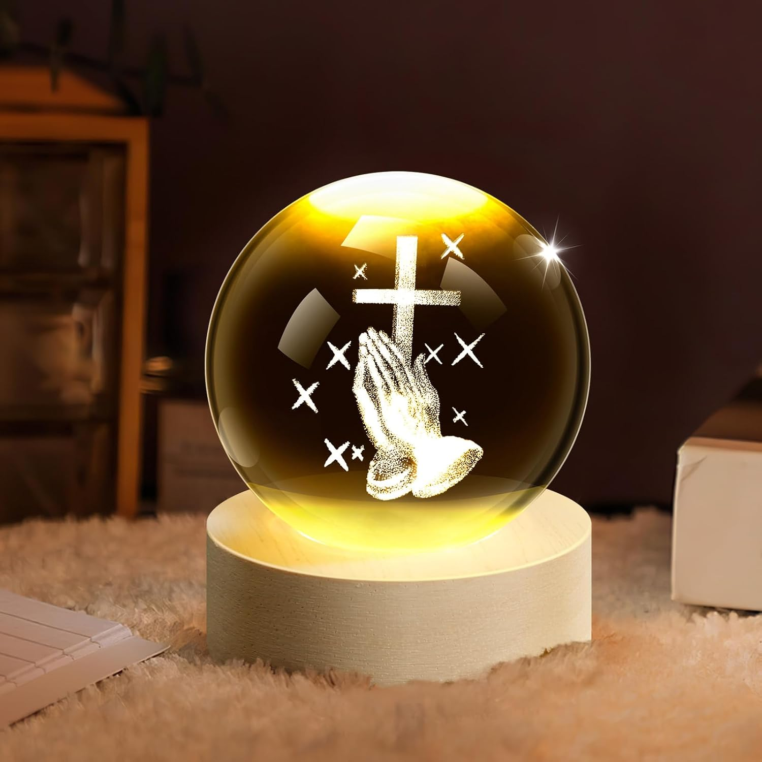 Kristallkugel mit betenden Händen und Kreuz, beleuchtet auf einem Holzsockel.