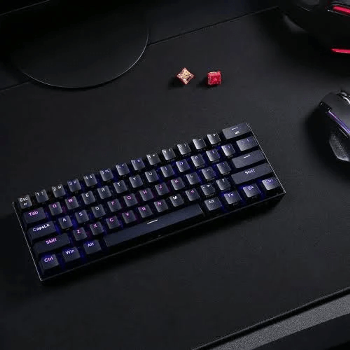 Un teclado mecánico negro con retroiluminación púrpura está sobre un escritorio junto a un ratón.