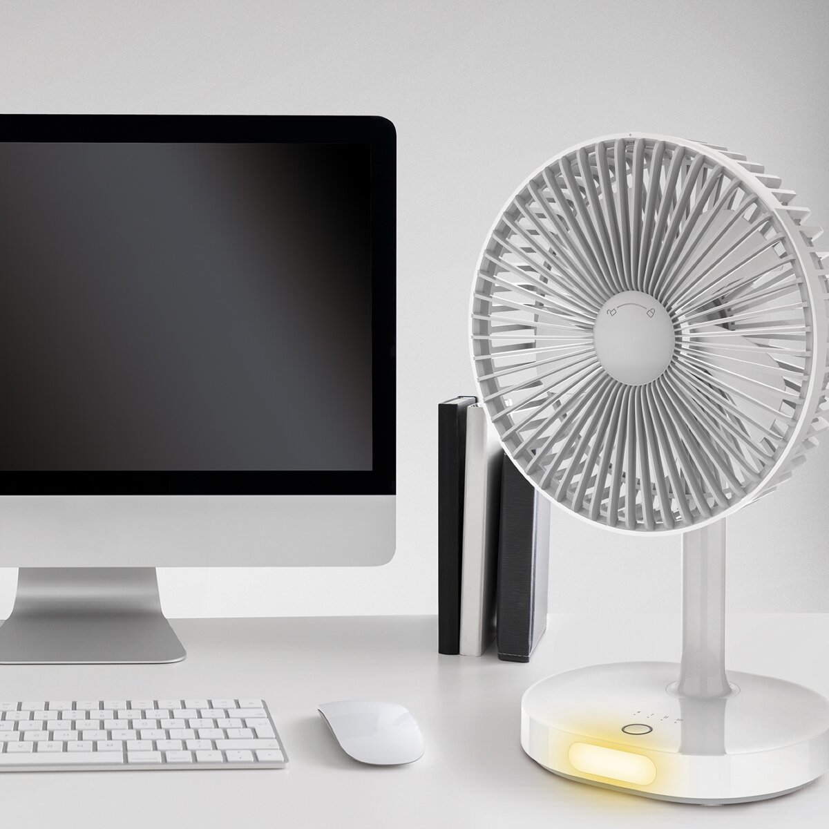 Ein weißer Schreibtisch mit Computer, Tastatur, Maus, Büchern und einem Ventilator.