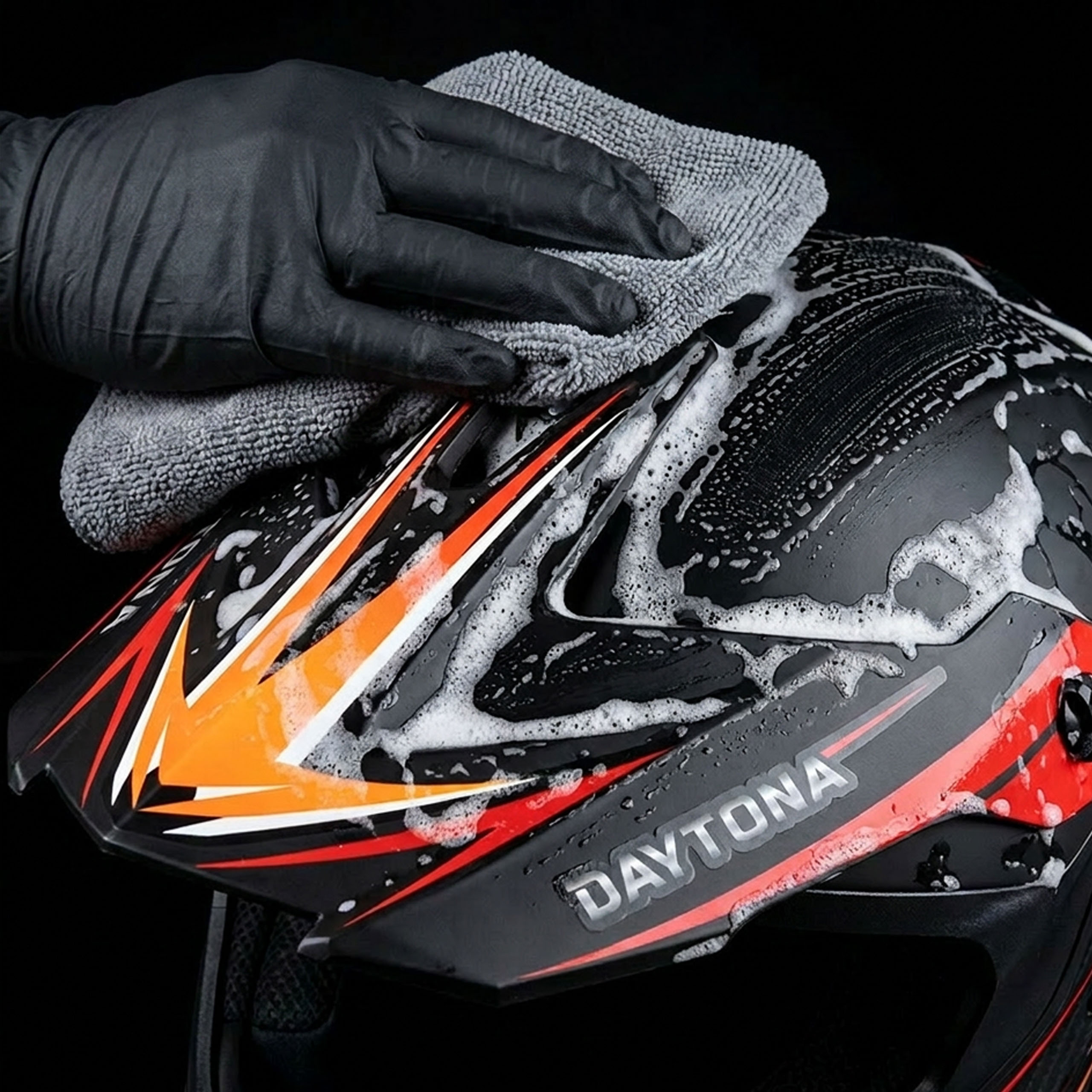 Casco moto nero e rosso con accenti arancioni pulito con panno in microfibra.