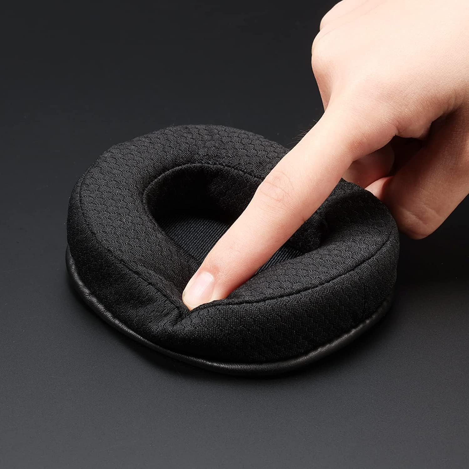 Un dedo presiona un auricular negro y acolchado sobre una superficie negra.