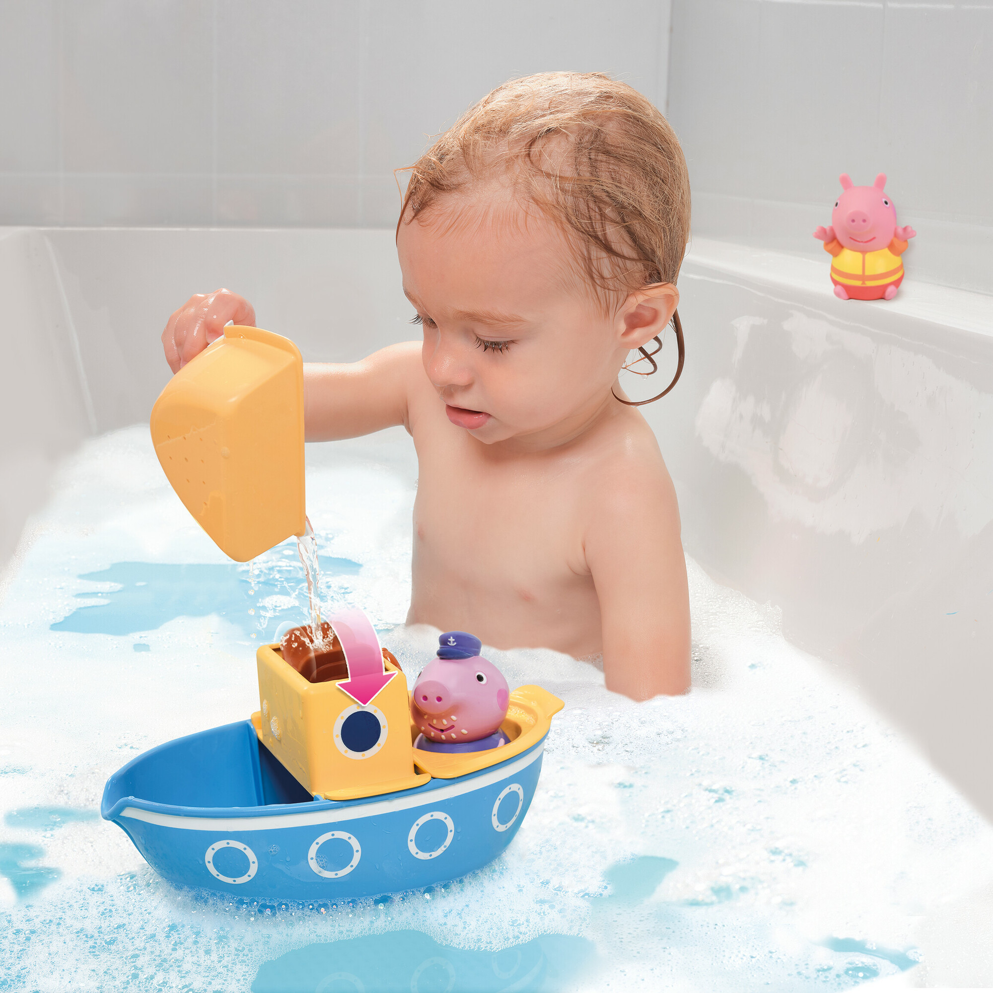 Ein Baby spielt mit einem Spielzeugboot in der Badewanne. Wasser fließt aus einem Becher.