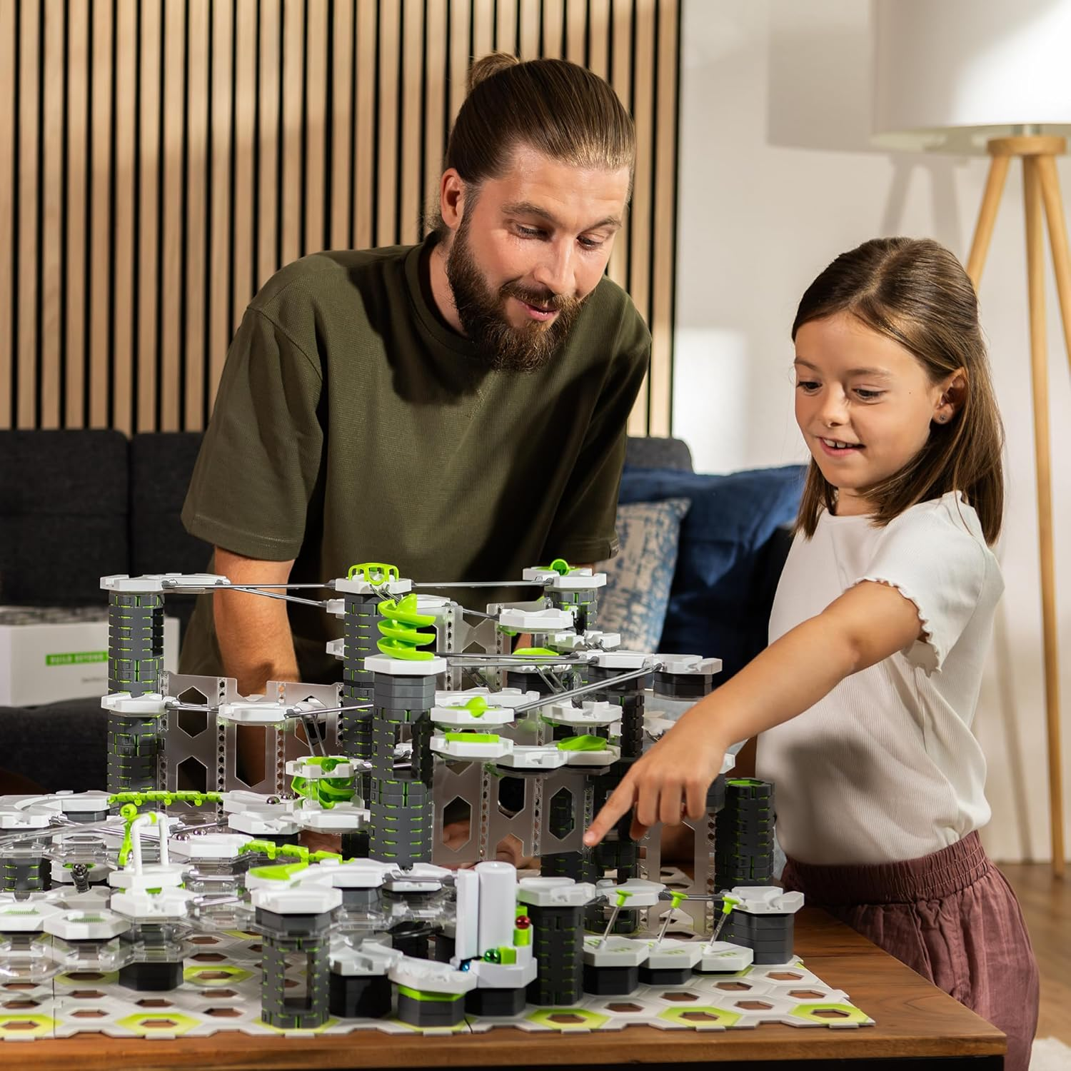 Ein Mann und ein Mädchen bauen ein komplexes Spielzeug mit grünen und grauen Teilen.