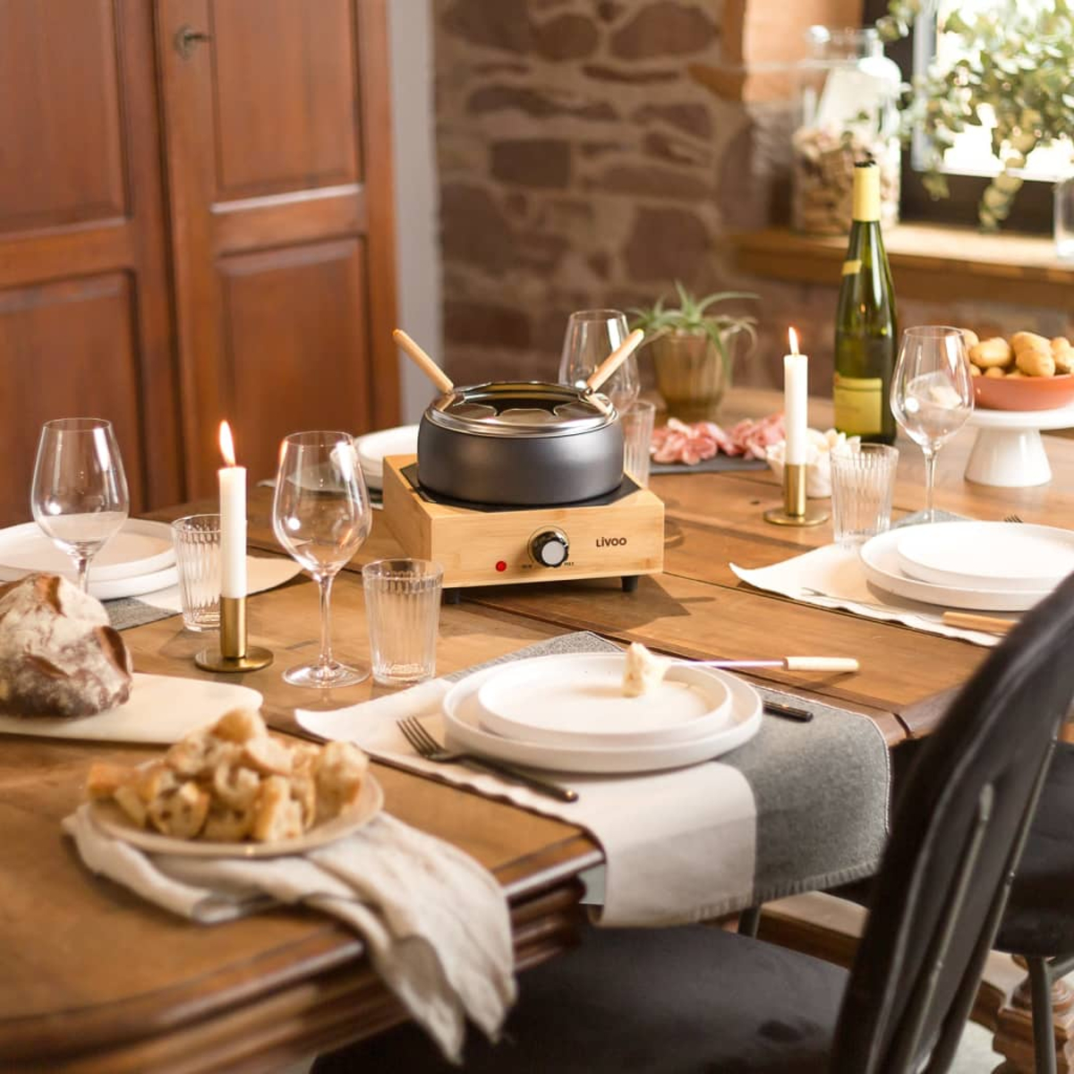 Un tavolo di legno è apparecchiato per una cena a base di fonduta, con candele, vino e pane.