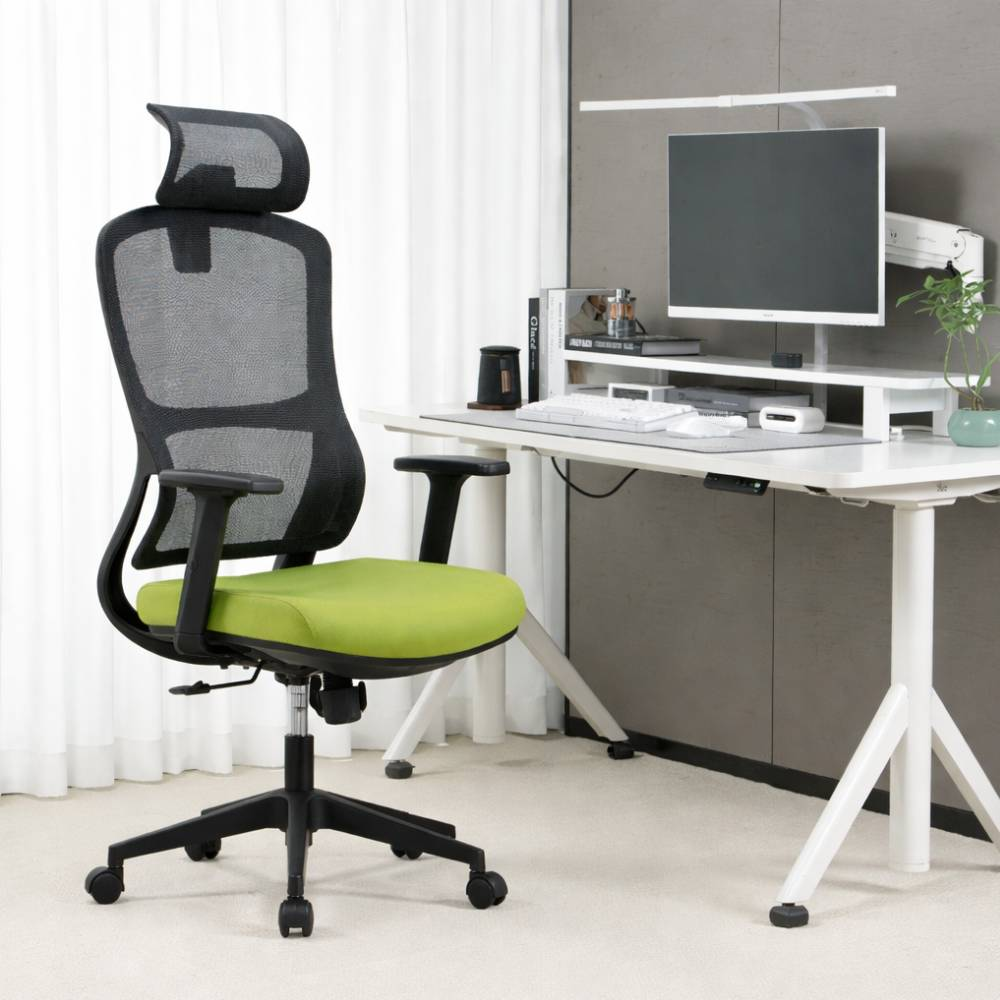Una sedia da ufficio nera con seduta verde chiaro davanti a una scrivania con monitor.