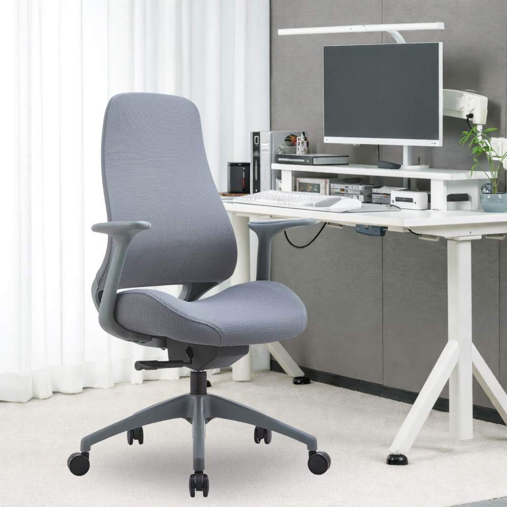 Una sedia da ufficio grigia con ruote si trova davanti a una scrivania bianca con monitor.