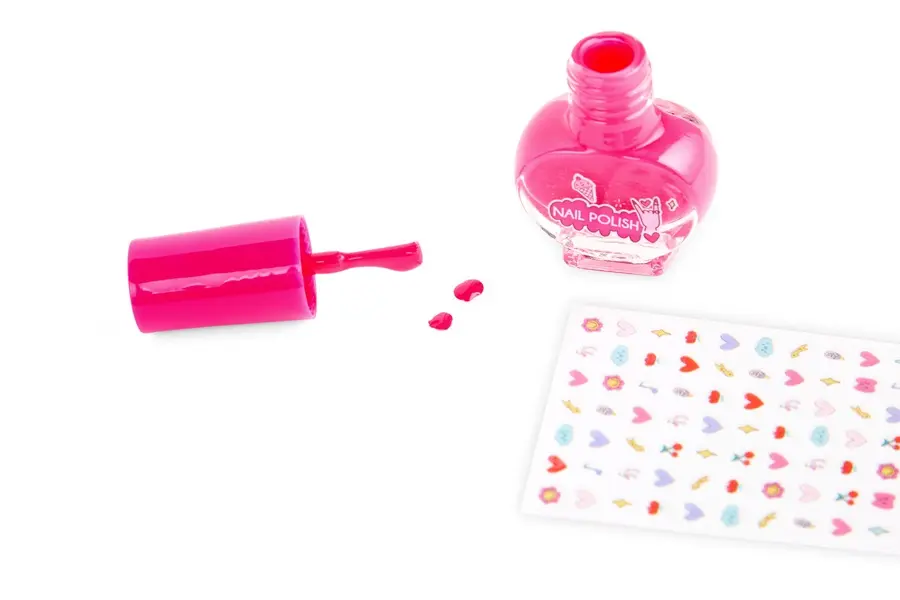 Botella de esmalte de uñas rosa, pincel y pegatinas sobre fondo blanco.