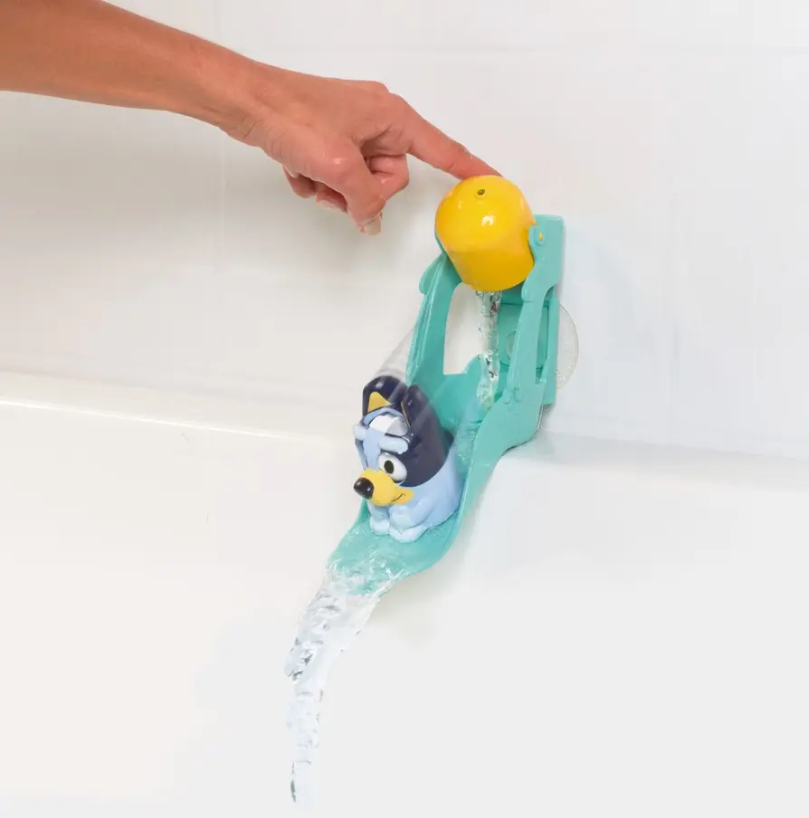 Una taza amarilla vierte agua en un tobogán turquesa con una figura de Bluey deslizándose en una bañera.