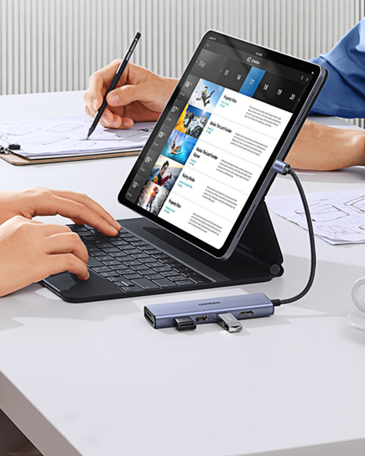 Masanın üzerindeki klavyeli ve USB hub'lı tablet, yazı yazan ve yazan eller.