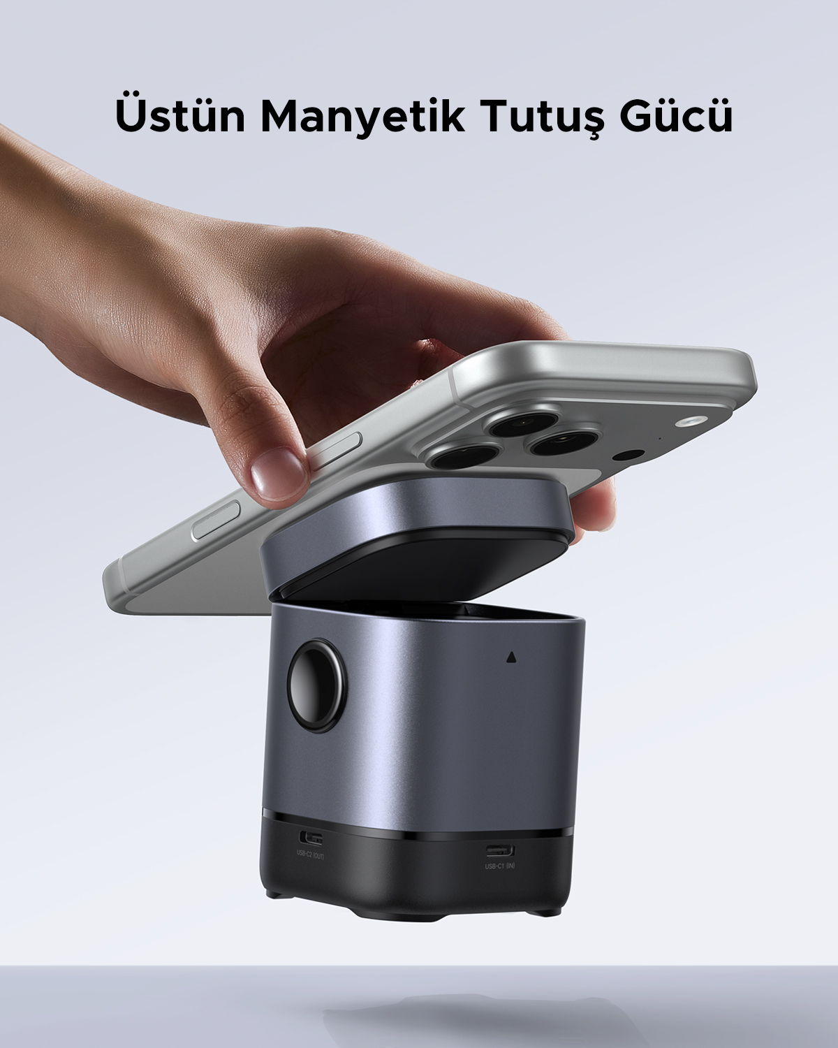 Bir el, USB bağlantı noktalarına sahip koyu renkli, silindirik bir cihazın üzerinde gümüş rengi bir akıllı telefon tutuyor.