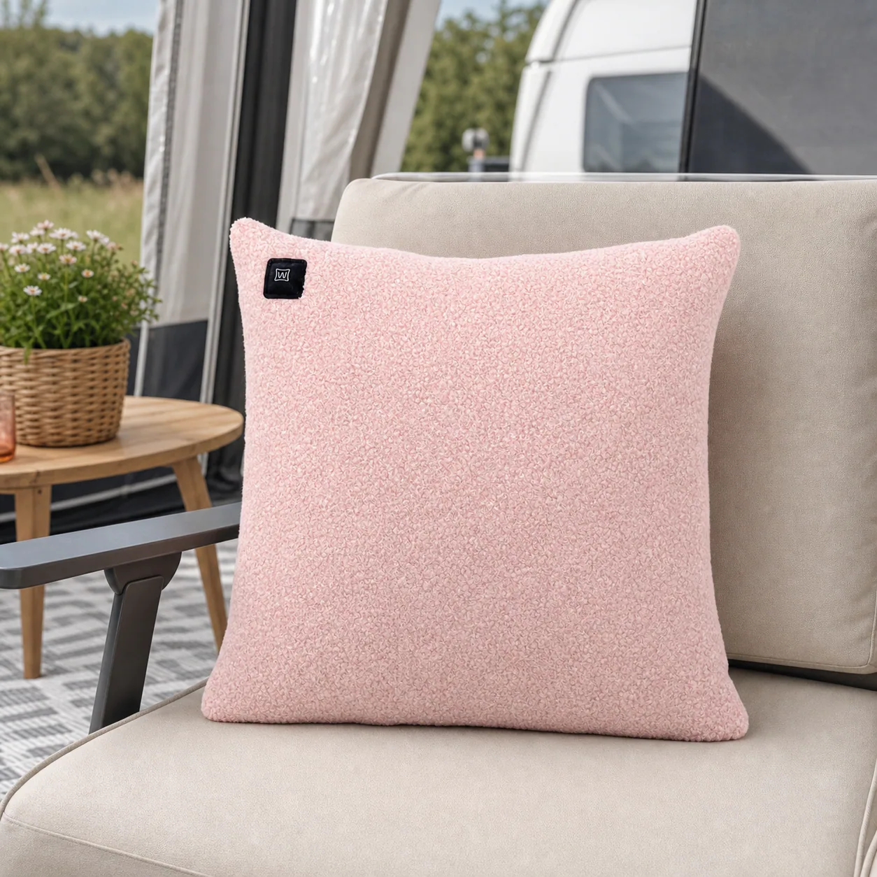 Ein rosafarbenes Kissen auf einem Sessel im Freien, mit einem Tisch und Blumen im Hintergrund.