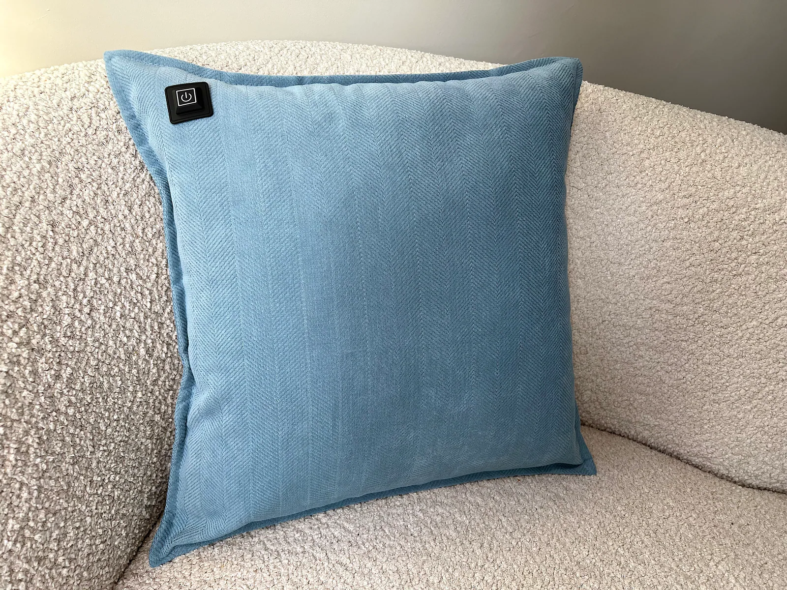 Ein blasses blaues Kissen mit Fischgrätmuster liegt auf einem cremefarbenen Sofa.