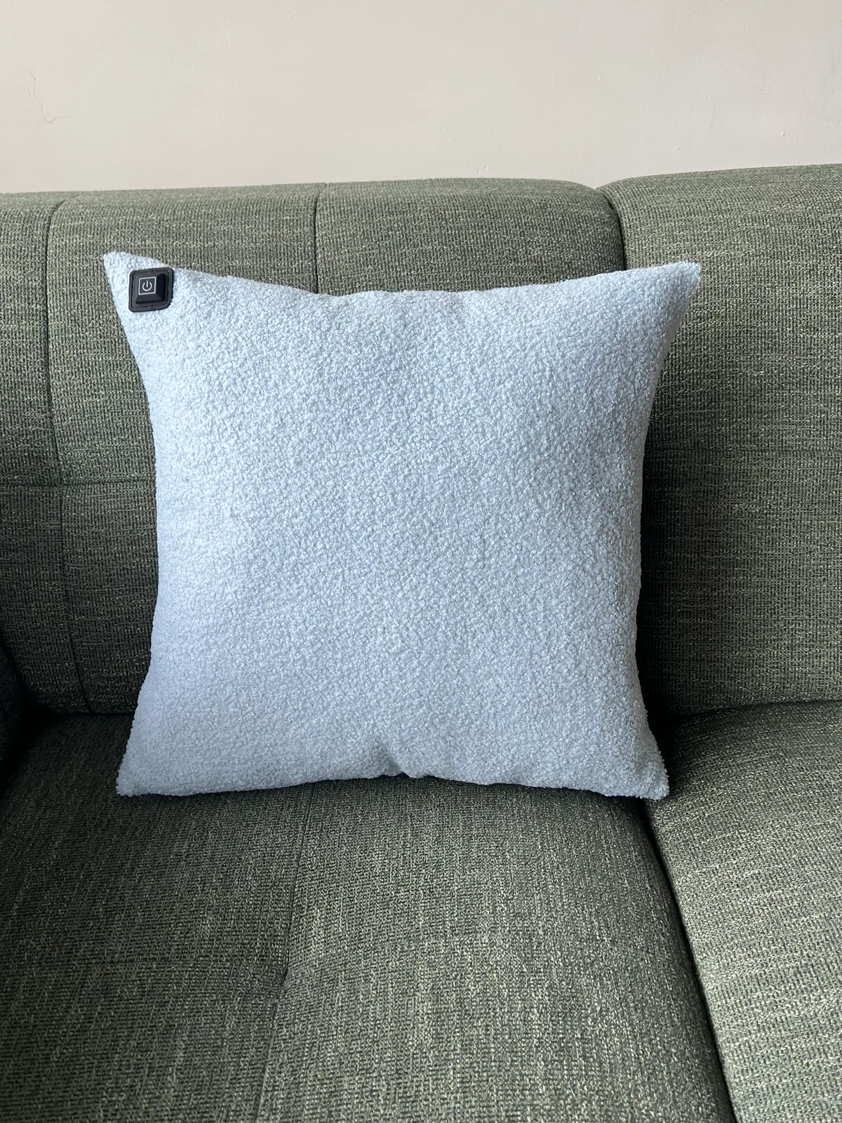 Ein hellblaues Kissen mit Heizfunktion liegt auf einem grünen Sofa.