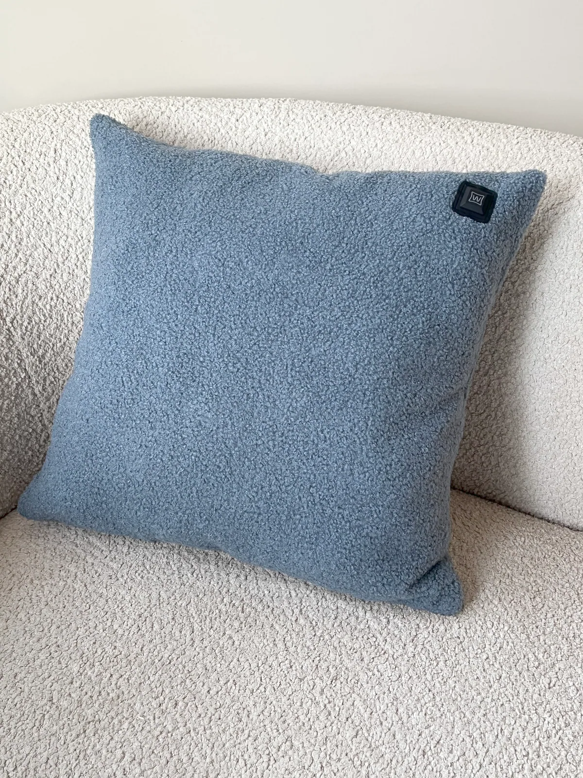 Ein blauer Teddy-Stoff-Kissen liegt auf einem cremefarbenen Bouclé-Sofa.
