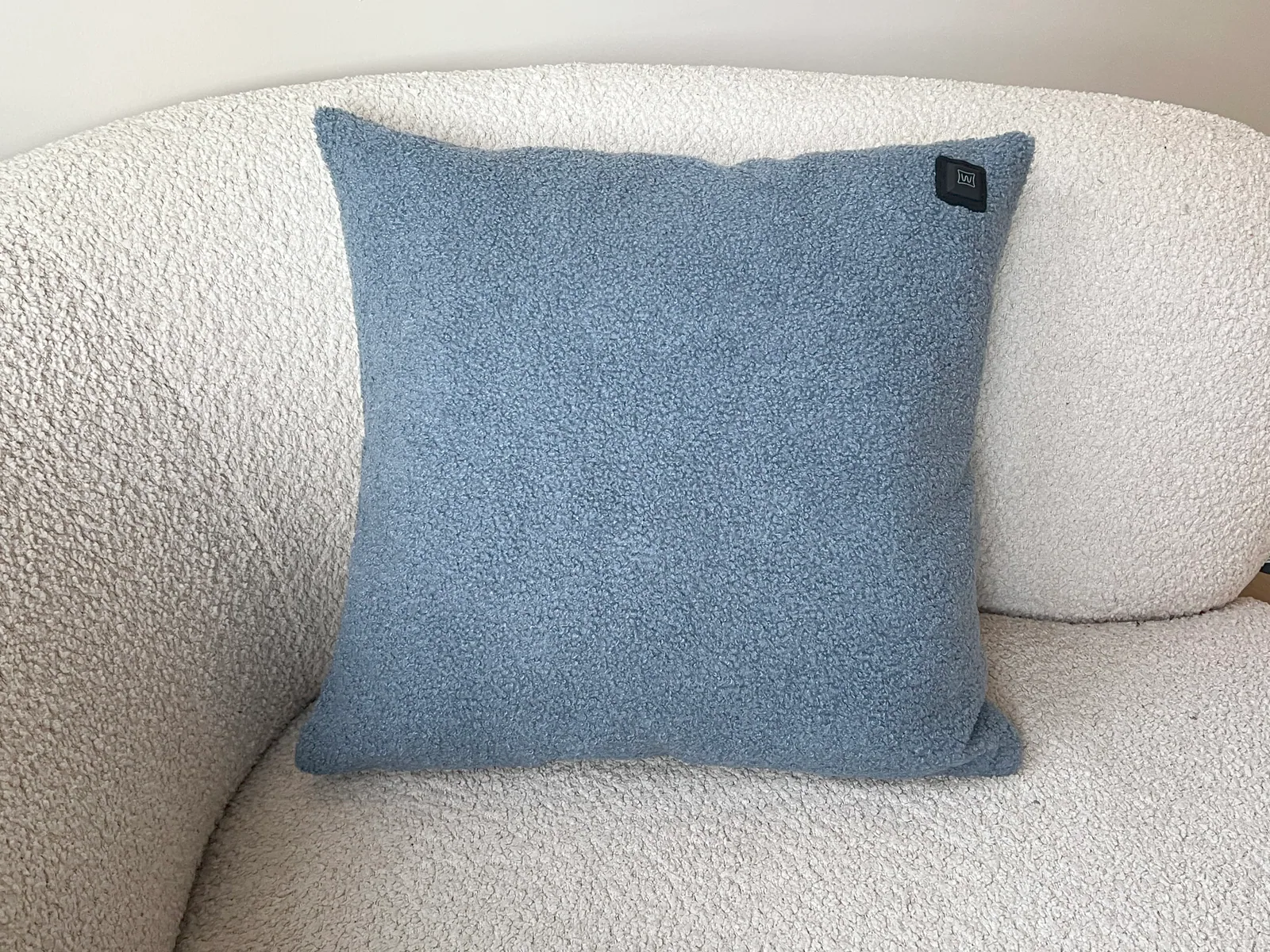 Ein blauer Bouclé-Kissen auf einem weißen Bouclé-Sofa.